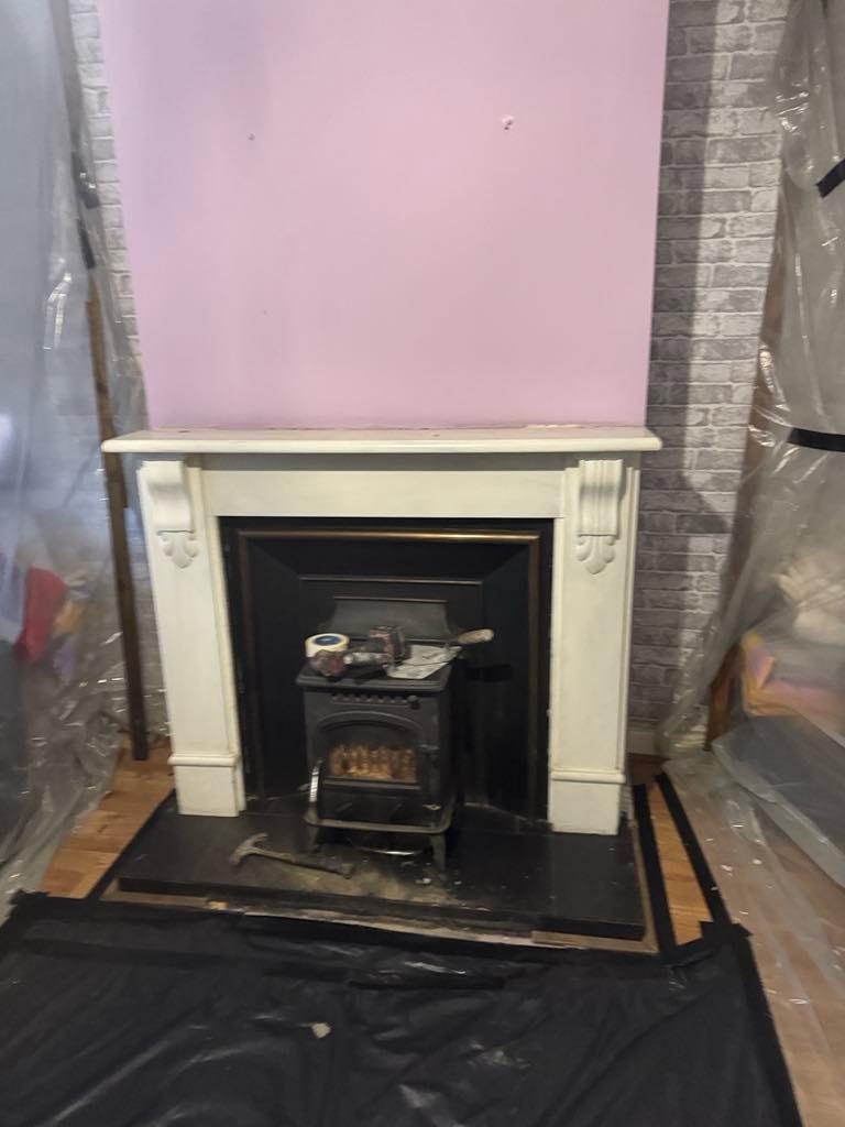 Old cast iron fireplace with painted surround before removal, room sheeted for dust protection